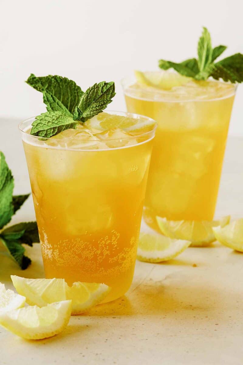 A close up of summer shandy cocktails with fresh mint and lemon wedges.