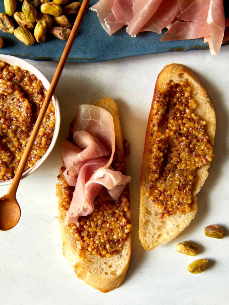 Homemade Whole Grain Mustard spread on some toast points with prosciutto on top.