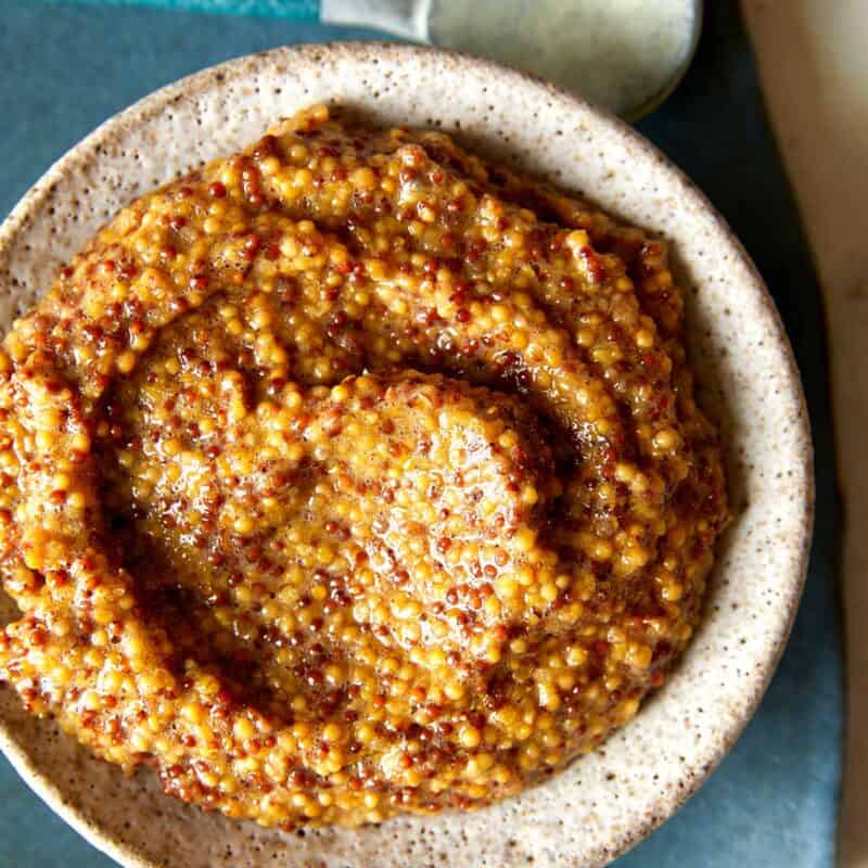 Homemade whole grain mustard in a bowl with a spoon next to it.