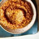 Homemade whole grain mustard in a bowl with a spoon next to it.