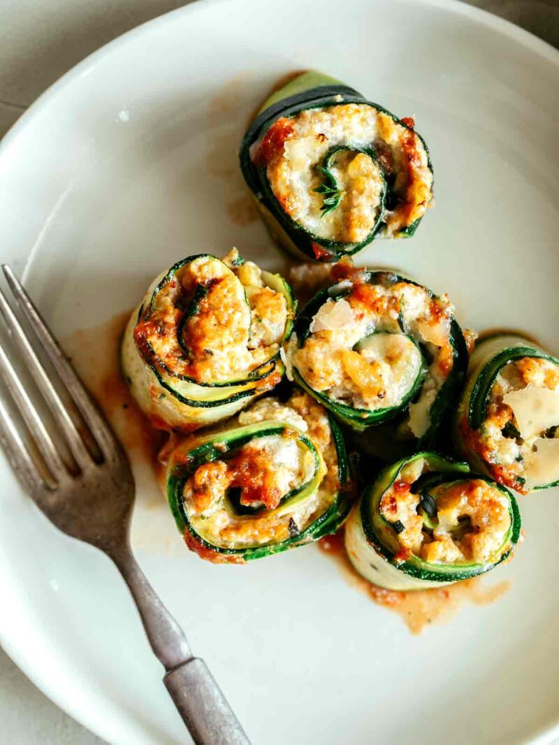 Six lasagna roll ups on a plate with a fork next to them. 