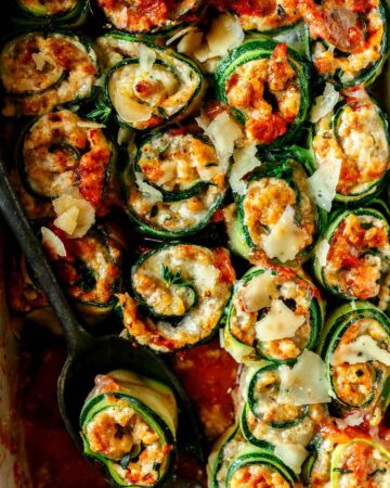 A close up of zucchini lasagna roll ups with a serving spoon.