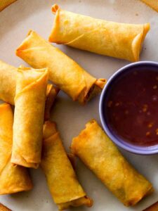 A close up on Vietnamese Style Pork and Shrimp Egg Rolls on a plate with sauce next to them.