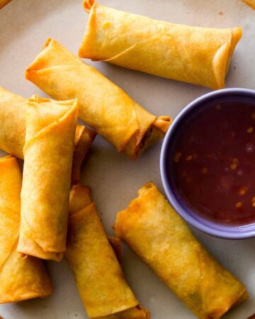 A close up on Vietnamese Style Pork and Shrimp Egg Rolls on a plate with sauce next to them.