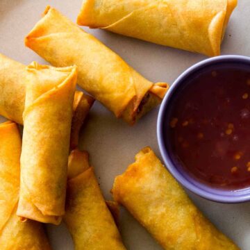 Egg rolls on a platter with a sweet and spicy sauce on the side.
