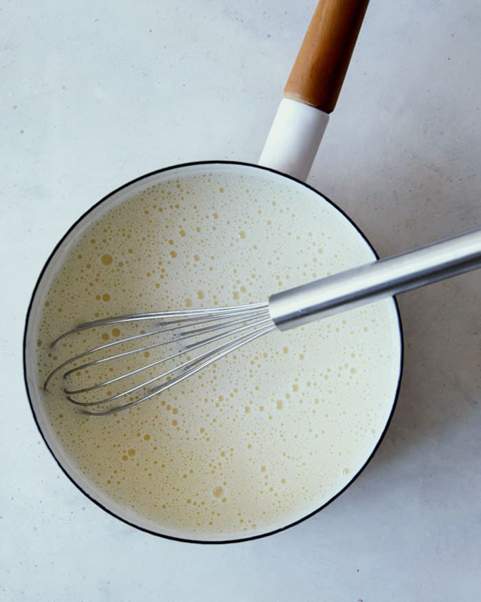 A pot shot overheat with a whisk in it showing how you add ingredients for banana pudding back into the pot.