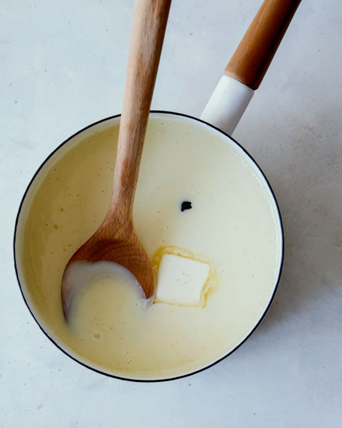 Adding butter and vanilla into a pot to make banana pudding recipe. 