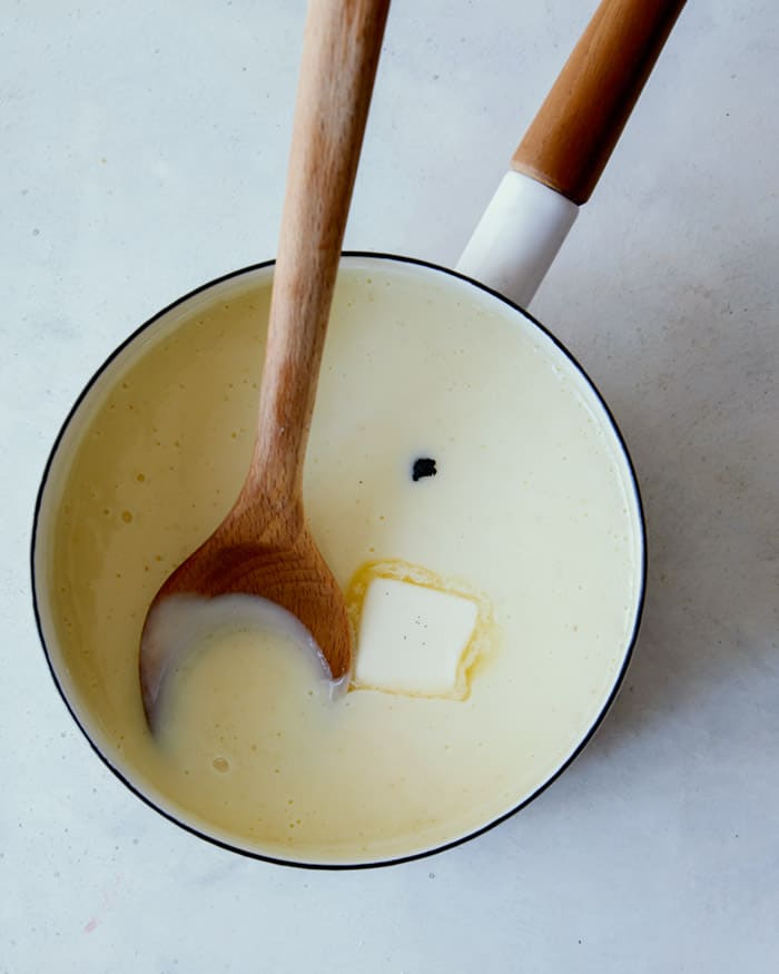 Adding butter and vanilla into a pot to make banana pudding recipe.