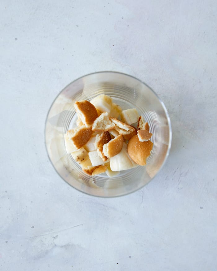 Adding crushed nilla wafers to a cup to make homemade banana pudding.