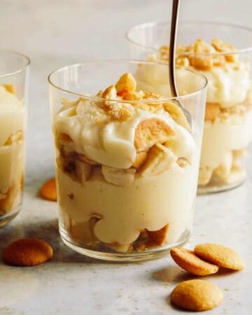 Three cups of banana pudding and one with a spoon in it.