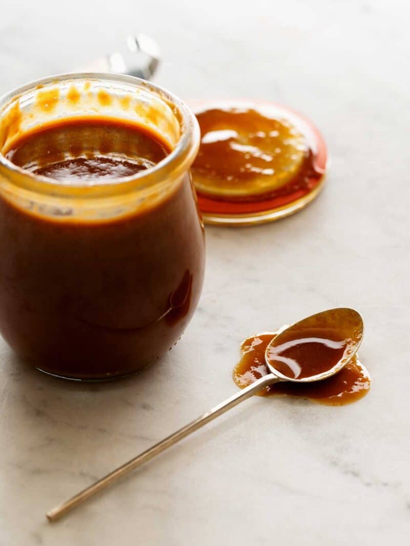 Cajeta in a jar with a spoon next to it with cajeta on it. 