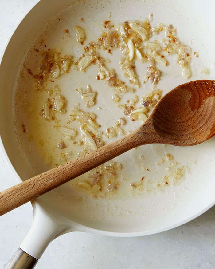 Sauted shallots and garlic in a skillet shot overhead with wooden spoon.