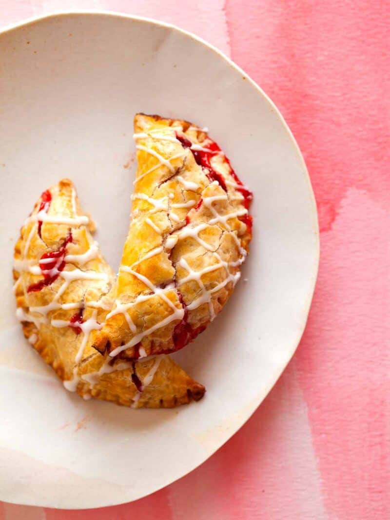 A close up of two cherry hand pies with cherry icing drizzle on a plate.