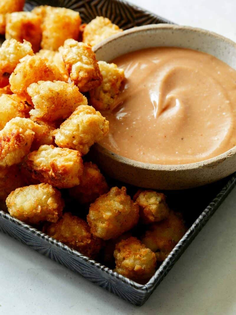 A bowl of homemade chick fil a sauce with a lot of tater tots on the side.