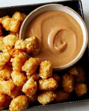 A bowl of homemade chick fil a sauce with a lot of tater tots on the side.