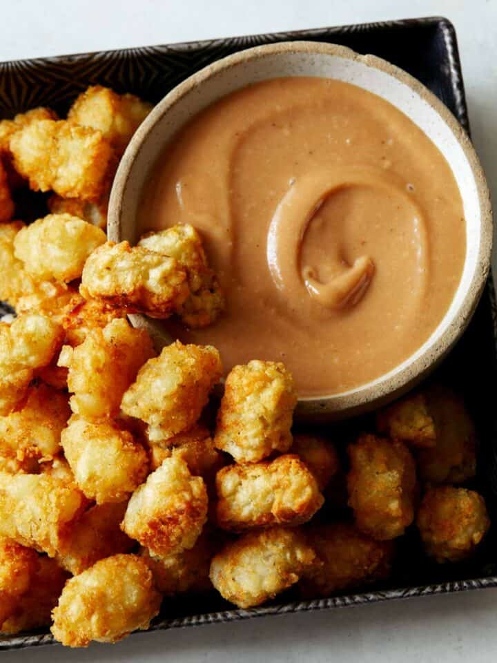 A bowl of homemade chick fil a sauce with a lot of tater tots on the side.