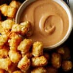 A bowl of homemade chick fil a sauce with a lot of tater tots on the side.