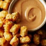 A bowl of homemade chick fil a sauce with a lot of tater tots on the side.