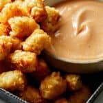 A bowl of homemade chick fil a sauce with a lot of tater tots on the side.