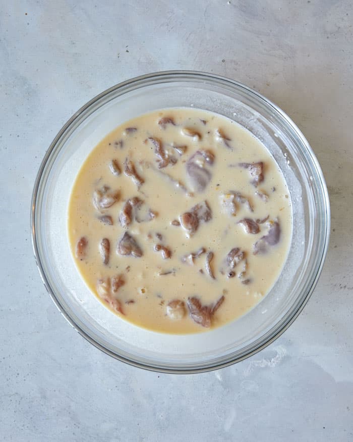 Batter for sesame chicken in a bowl with seasoned chicken thighs.