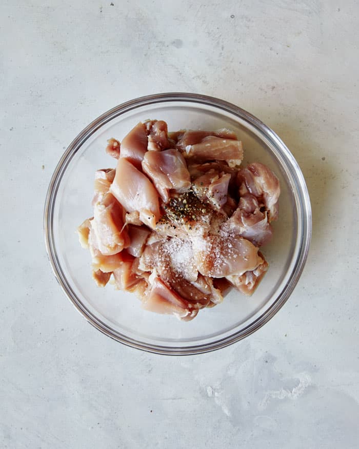 Chicken thighs in a bowl with salt and pepper on top.