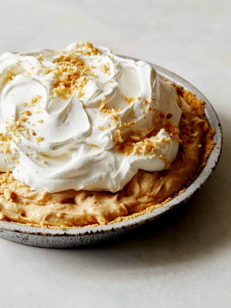 A close up on a creamy peanut butter pie with whipped cream, and nuts on top. 