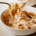 A bowl of fettuccine alfredo with a fork lifting some pasta out of it.