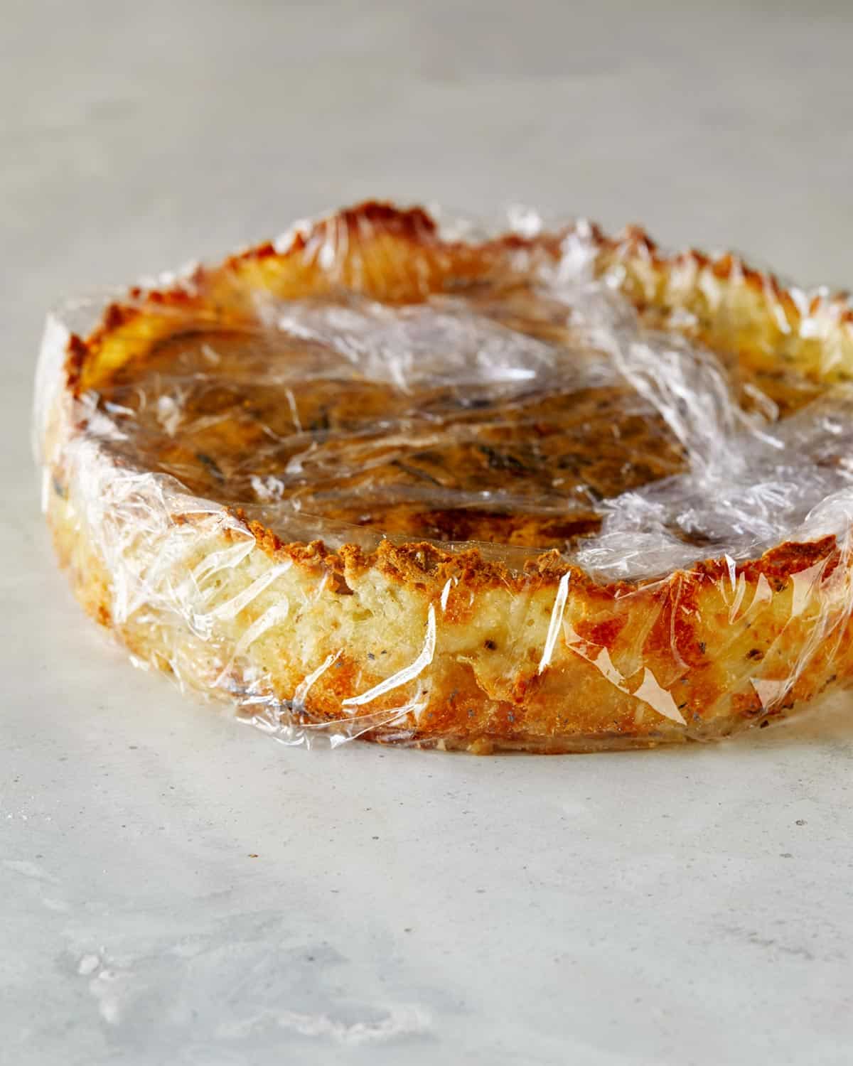 A hash brown quiche that is wrapped in plastic wrap. 
