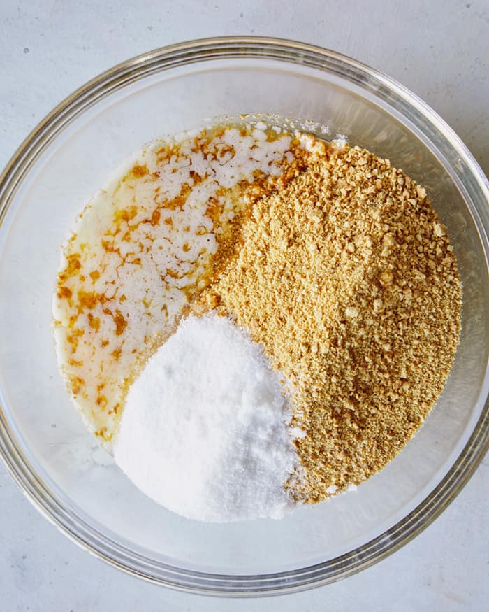 A glass bowl that has all of the ingredients for the graham cracker crust combined.
