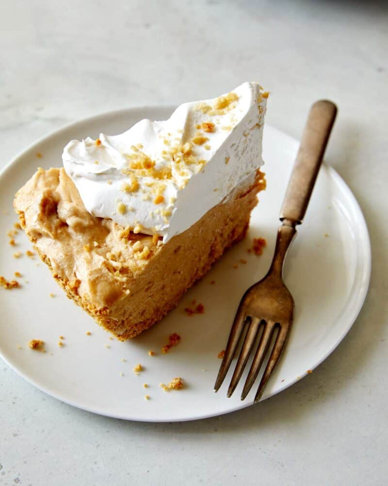 A slice of Creamy No Bake Peanut Butter Pie on a plate with a fork next to it.