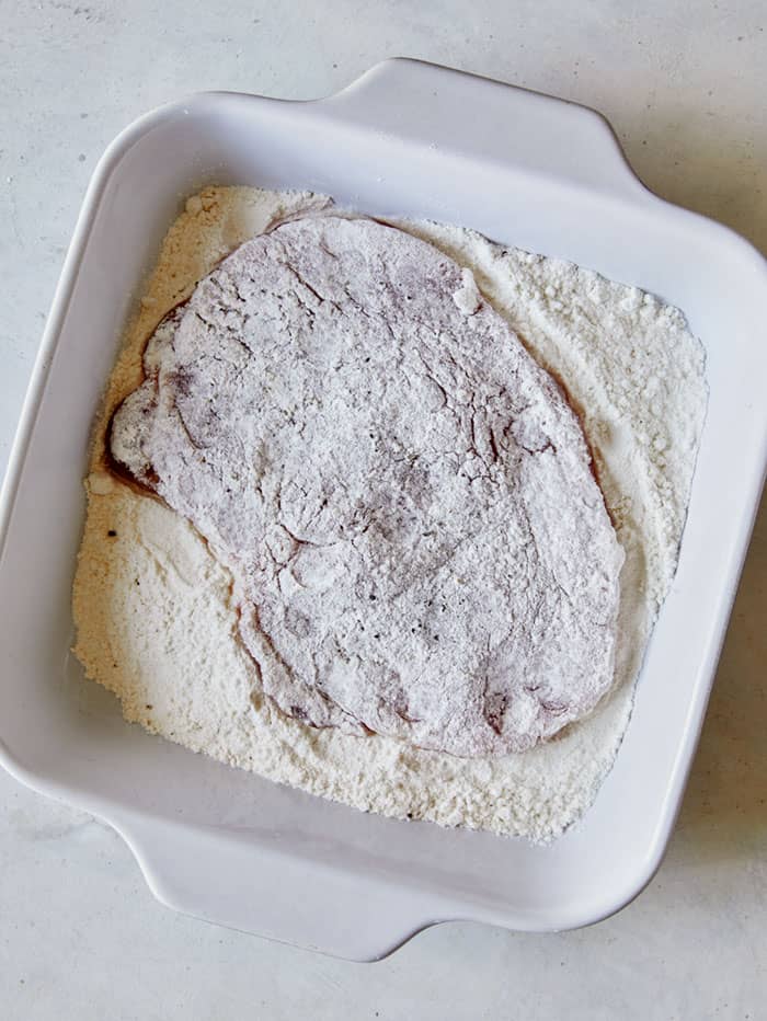 Pork tenderloin in a baking dish of flour.