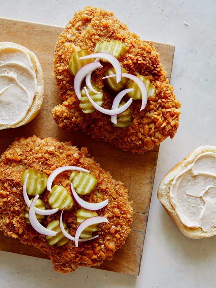 Building a pork tenderloin sandwich with pickles and onions on top of the cutlet.