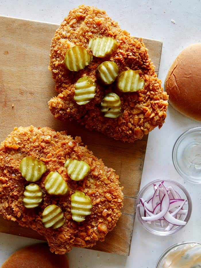 Building a pork tenderloin sandwich with pickles on top of the cutlet.