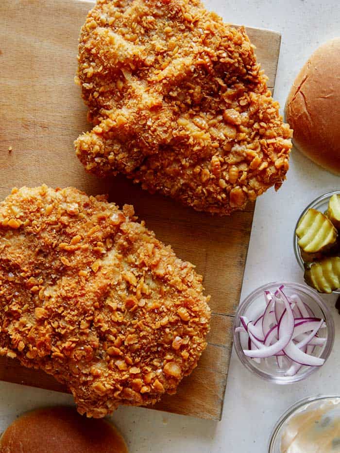 Pork cutlets on a cutting board with toppings next to it.