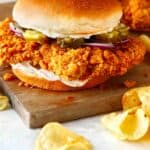 Pork Tenderloin sandwich on a cutting board with potato chips.