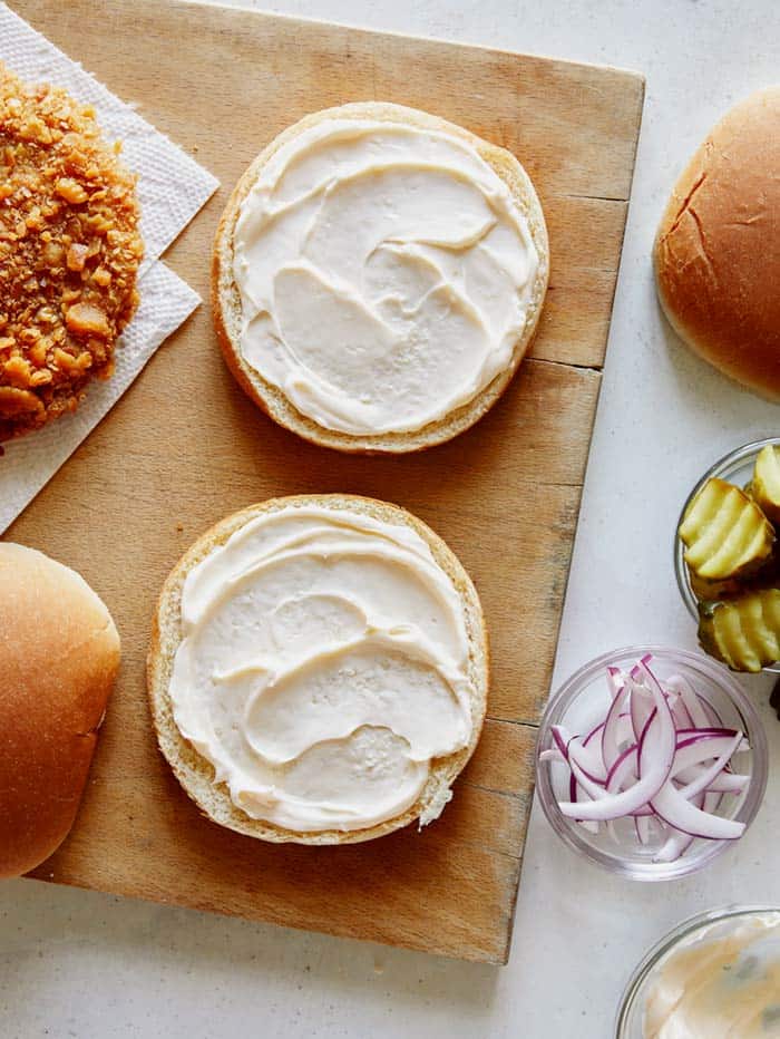 Two buns with mayonnaise spread on them and pork cutlets next to them.
