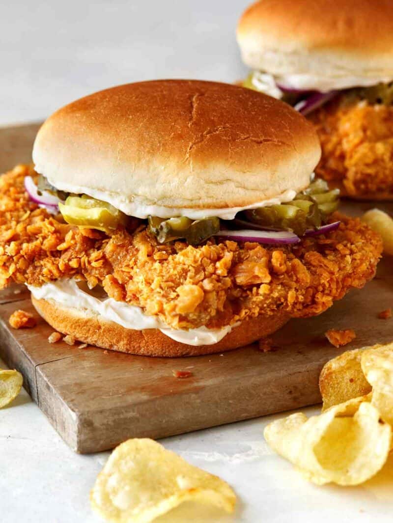 Pork Tenderloin sandwich on a cutting board with potato chips.