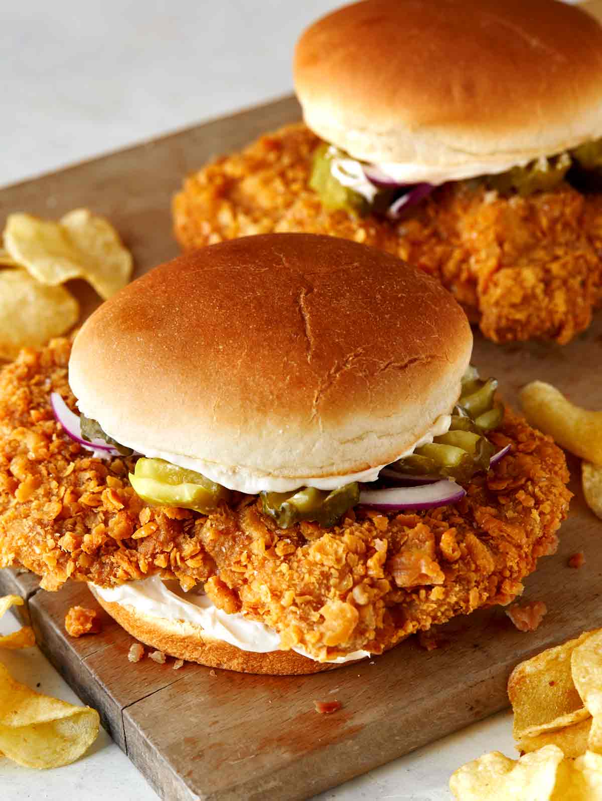 Two pork tenderloin sandwiches on a cutting board. Potato chips on the side.