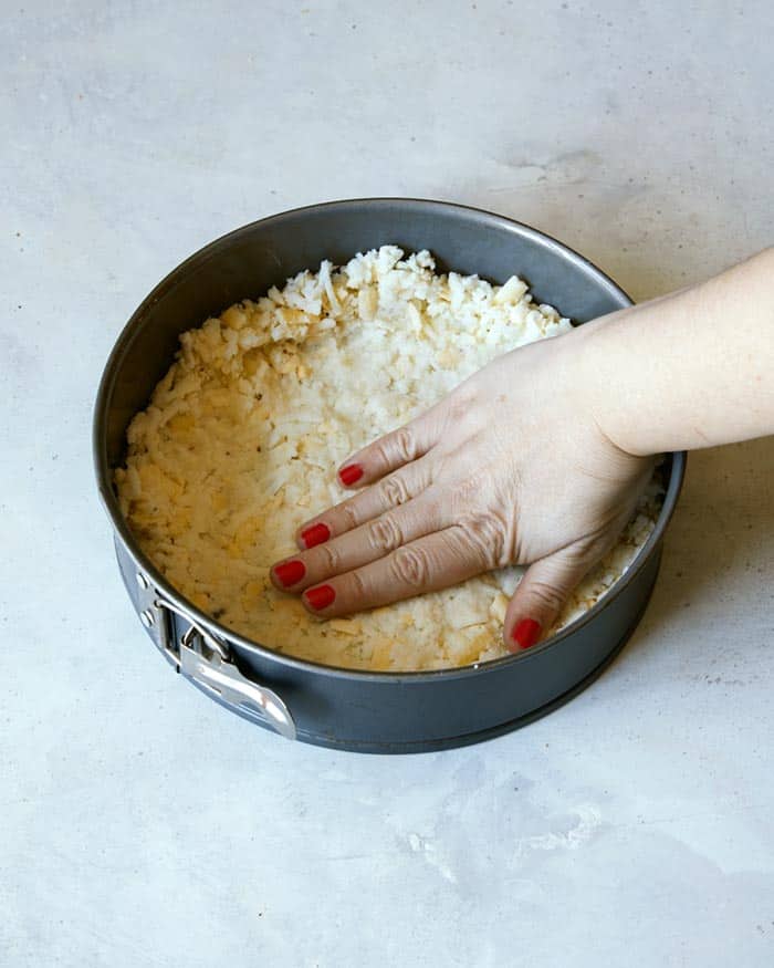 Hash brown crust mixture being pressed into a spring form pan.