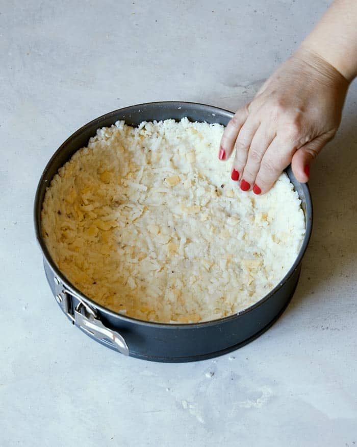Hash brown crust mixture being pressed into a spring form pan on the edges.