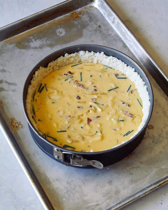 Quiche with a hash brown crust and filling on a baking sheet ready to be baked.
