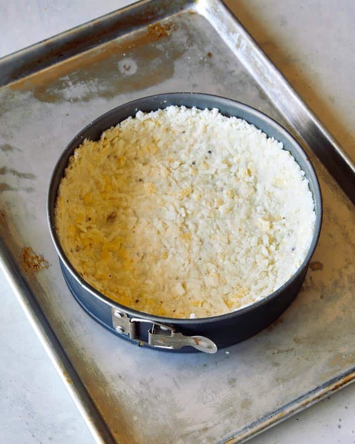 A spring form pan filled with a hash brown crust on a baking sheet. 