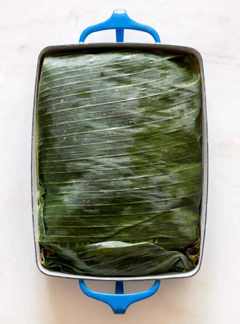 A pan of cochinita pibil wrapped in banana leaves.