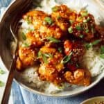 Sesame chicken in a bowl over rice with sesame seeds on the side.