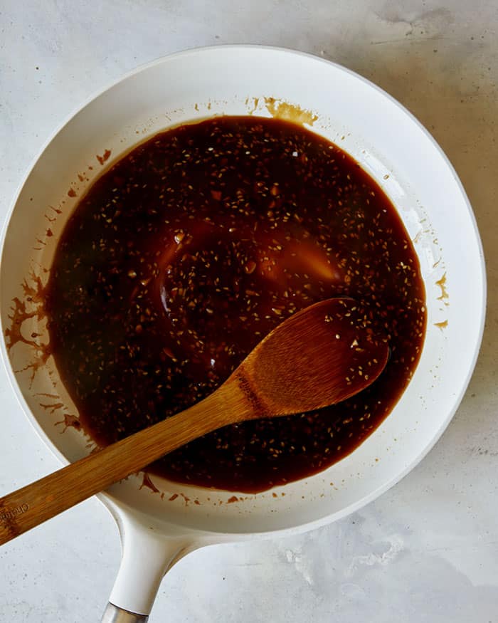 Sweet and sticky sesame chicken sauce in a skillet with a wooden spoon.