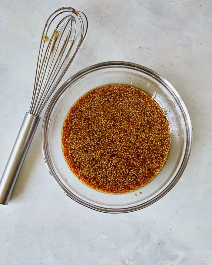 A bowl of sesame chicken sweet and sticky sauce in a mixing bowl with a whisk next to it.