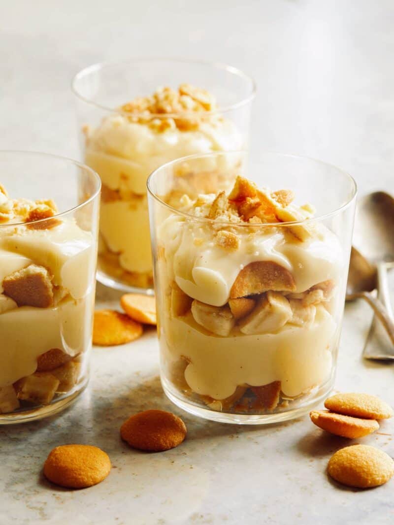 Three cups of banana pudding with nilla waffers on the side and spoons next to them.