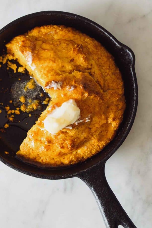 Pumpkin cornbread in a skillet with butter on top and honey.