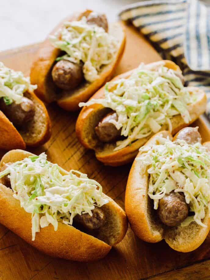 Bratwursts topped with slaw on a cutting board.
