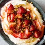 Honey whipped ricotta in a bowl topped with roastes strawberries and pistachios.